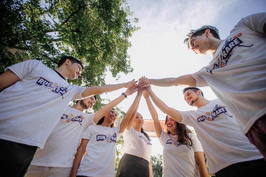 A group of young adults in white shirts sharing a joyful team moment outdoors.